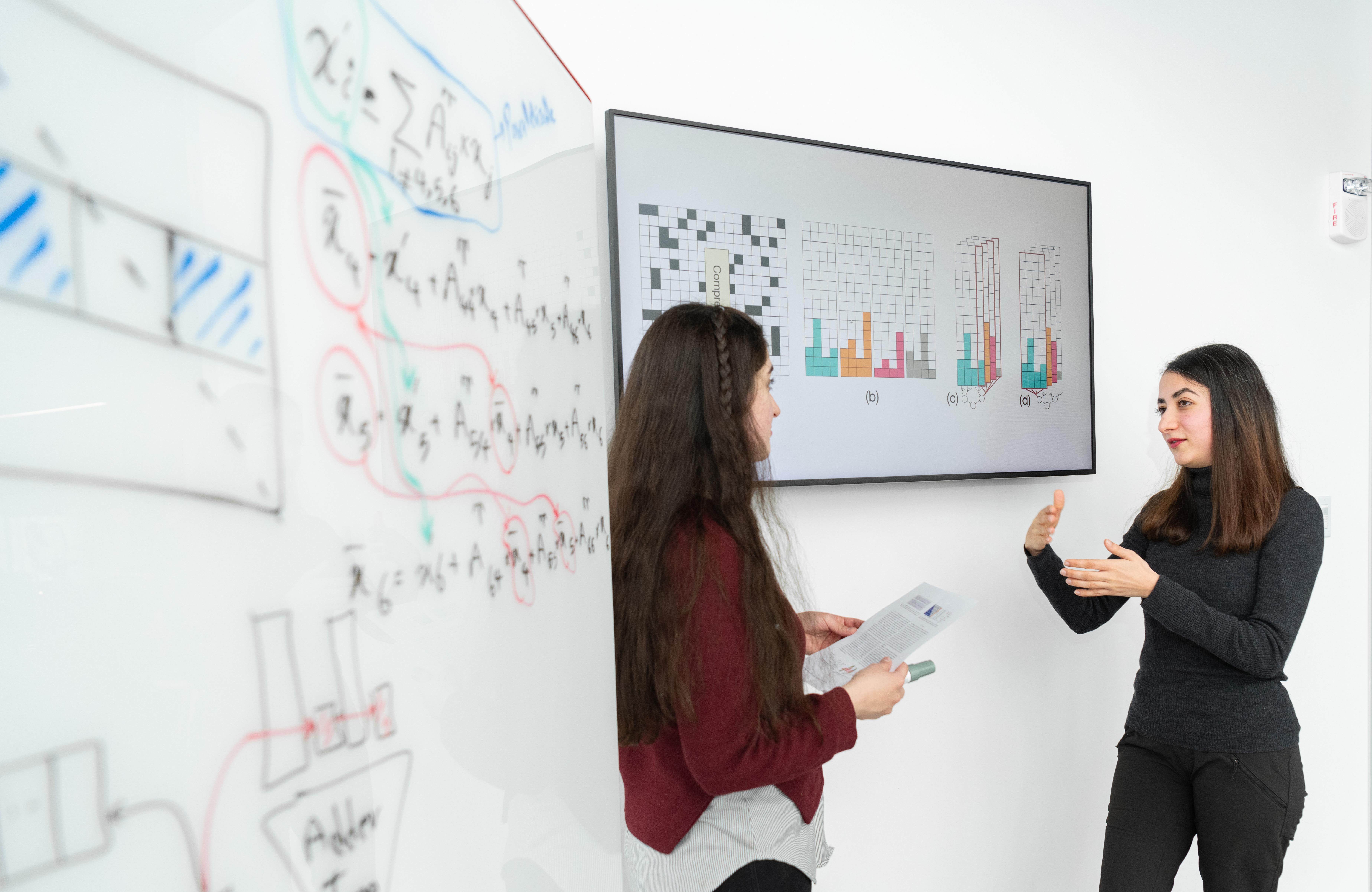 women discussing data next to whiteboard