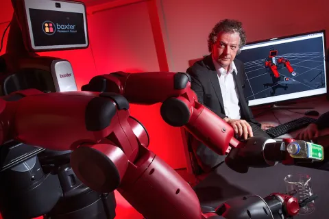 Yiannis Aloimonos sits with a Baxter Research Robot next to him. 