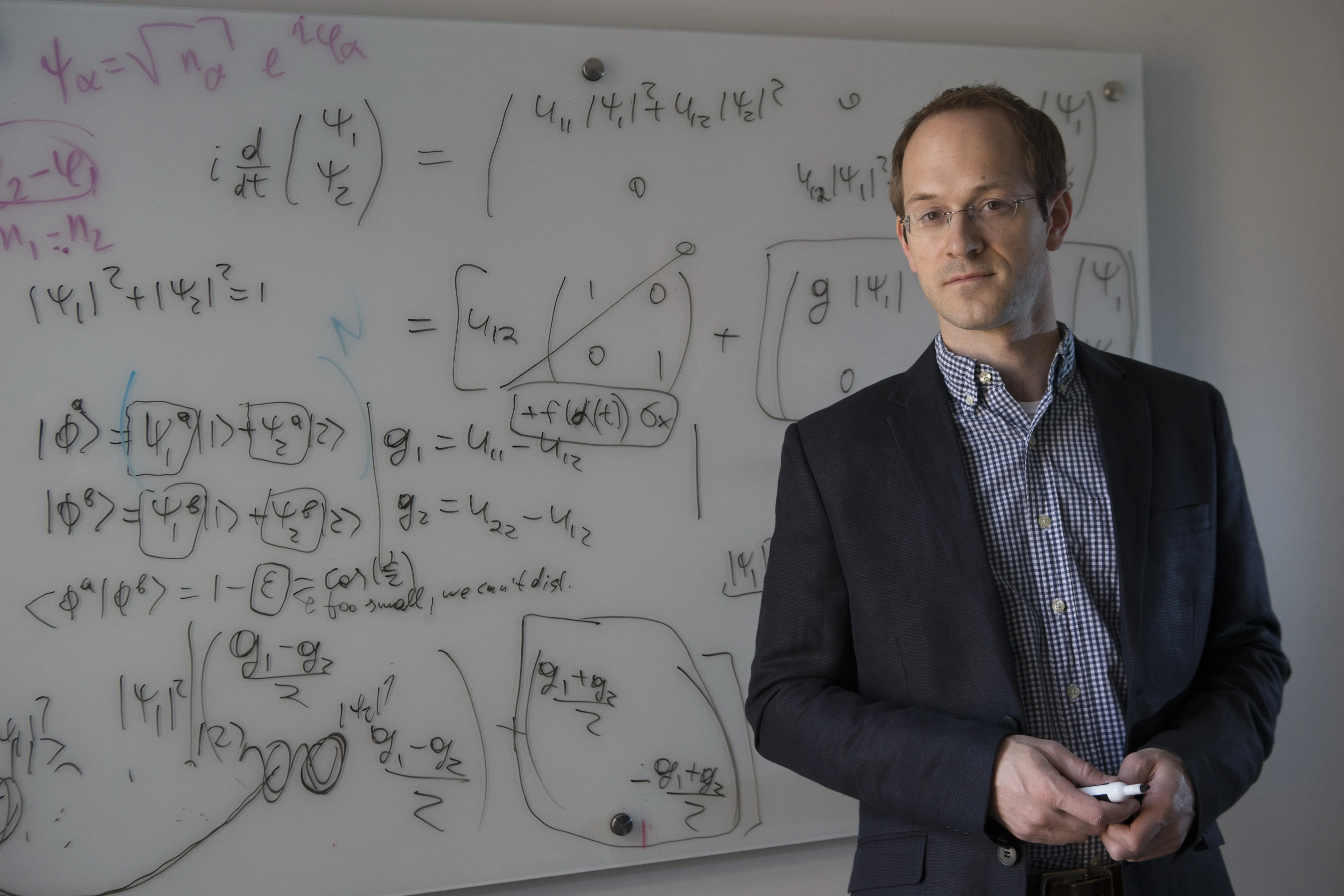 A photo of Andrew Childs in front of a white board with numerous equations written on it.